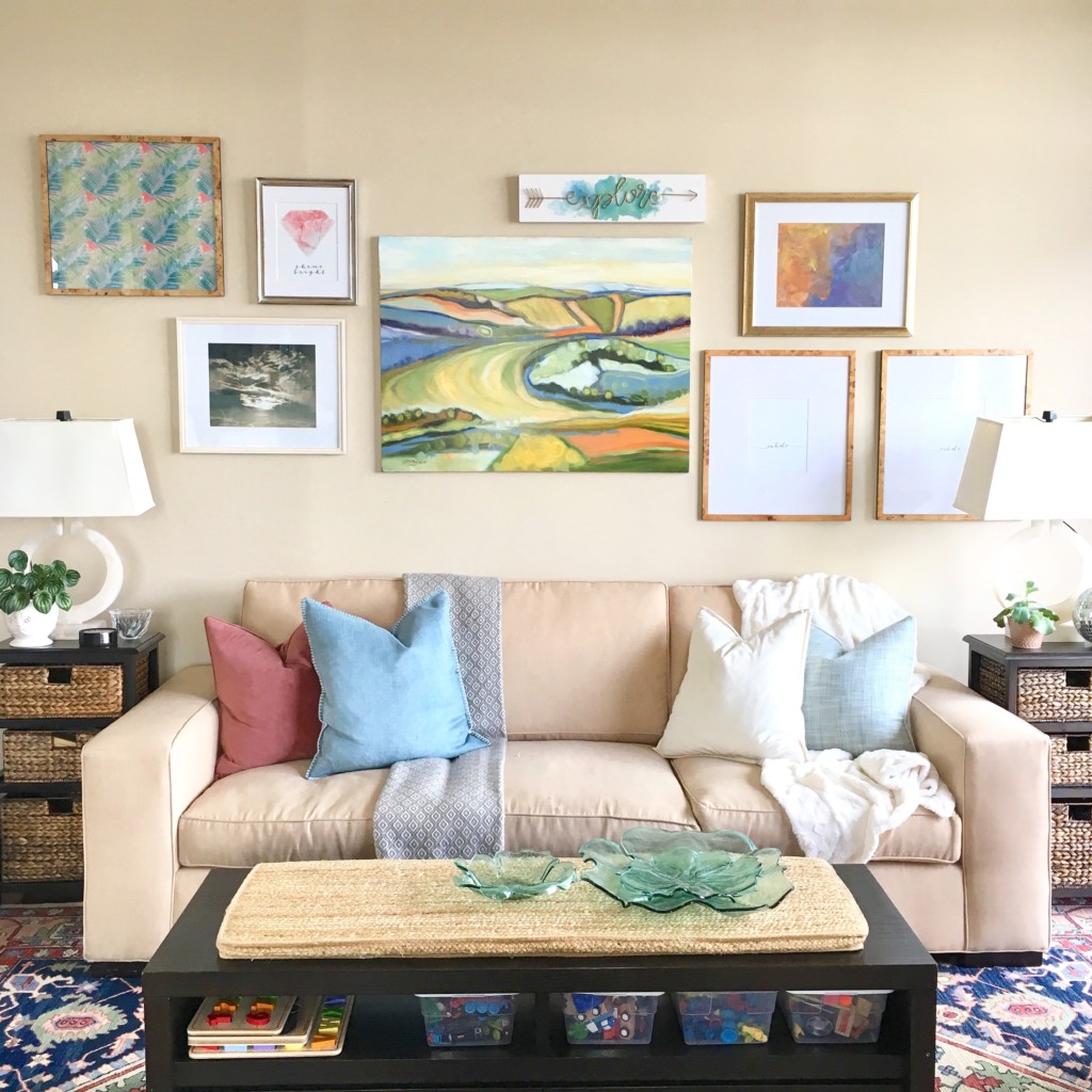 A bright and cheerful family room showcases a colorful gallery wall behind the cream colored couch.